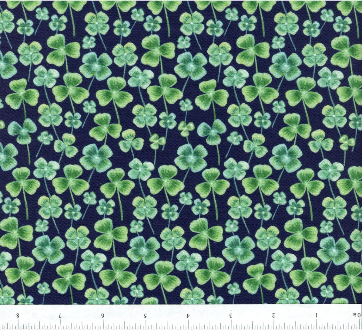 A yardstick measuring the fabric with a printed design featuring cats and leaves in green, red, and white colors, indicating a festive pattern likely for Easter and St. Patrick's Day crafts.